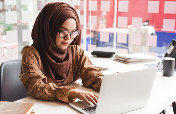 Young asian muslim business woman in smart casual wear working with laptop computer while sitting in the creative cafe.