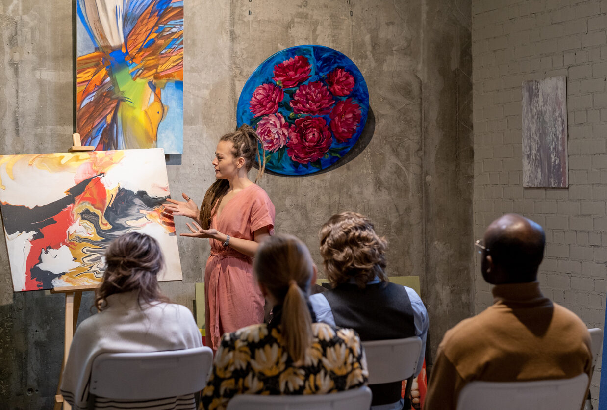 Young woman pointing at painting and presenting the modern art for people during presentation in art gallery