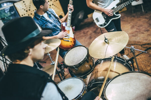 Repetition of rock music band. Cropped image of bass guitar player, electro guitar player and drummer behind the drum set. Rehearsal base